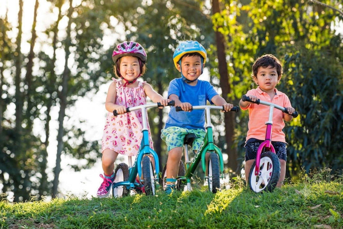 Three children on balance bikes in a park with trees in the background